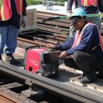 Worker adjusting a red Honda inverter generator at a rail work site